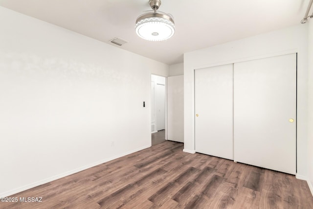 unfurnished bedroom featuring visible vents, baseboards, wood finished floors, and a closet
