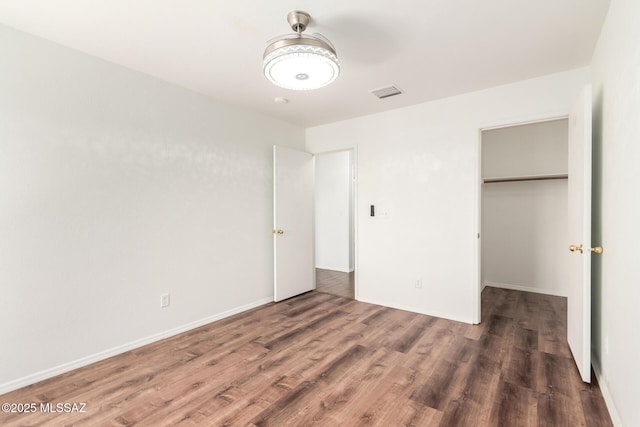 unfurnished bedroom with a walk in closet, baseboards, wood finished floors, visible vents, and a closet