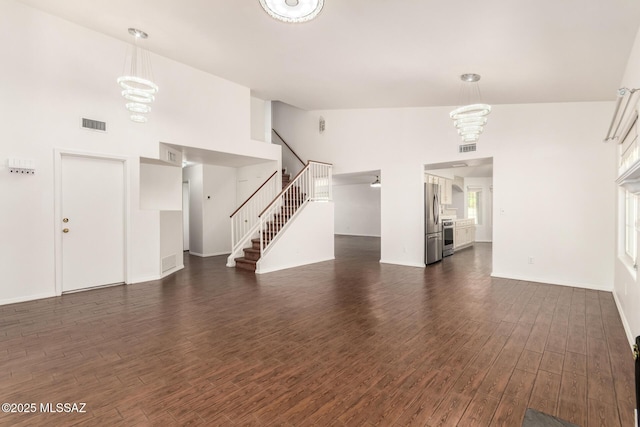 unfurnished living room featuring visible vents, dark wood-style floors, a chandelier, and stairs
