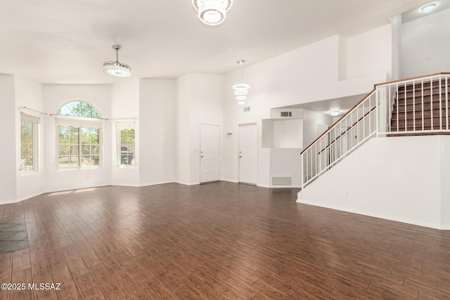 unfurnished living room featuring a towering ceiling, visible vents, stairway, baseboards, and dark wood-type flooring