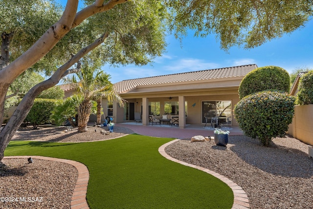 back of house featuring a tiled roof, stucco siding, ceiling fan, a patio, and a lawn