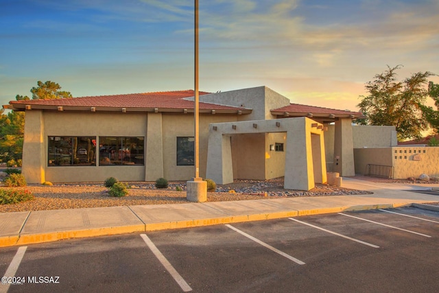 view of front of property with stucco siding, a tiled roof, uncovered parking, and fence