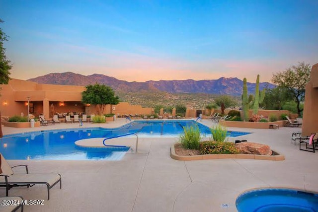 pool at dusk with a community pool, a mountain view, a hot tub, and a patio area