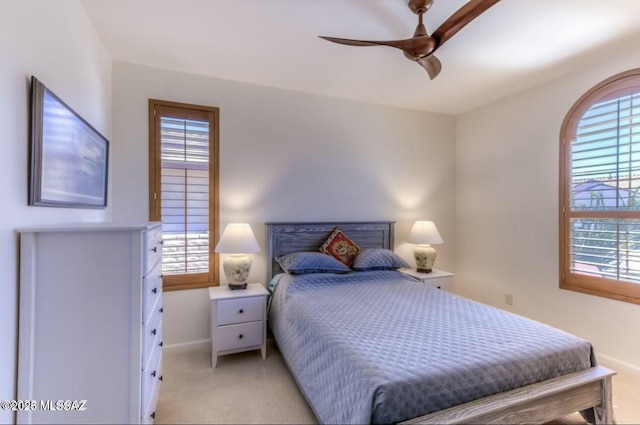 bedroom featuring light carpet, a ceiling fan, baseboards, and multiple windows
