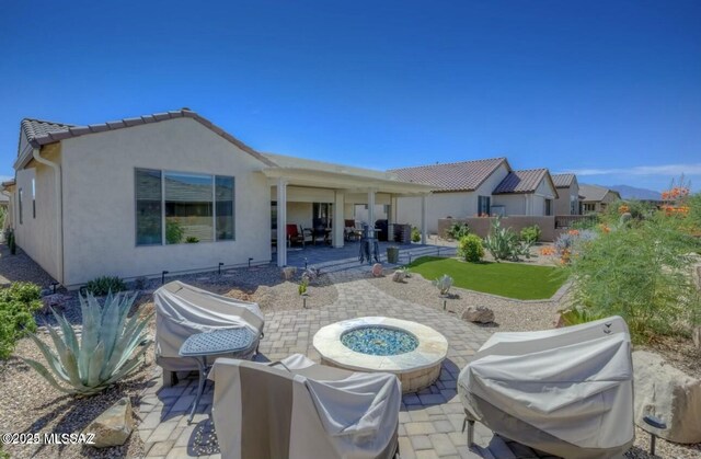 rear view of property featuring a fire pit, a patio, and stucco siding