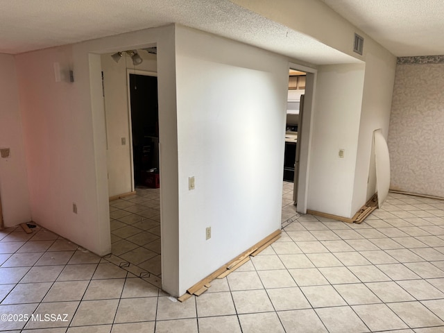 spare room with visible vents, a textured ceiling, baseboards, and light tile patterned floors