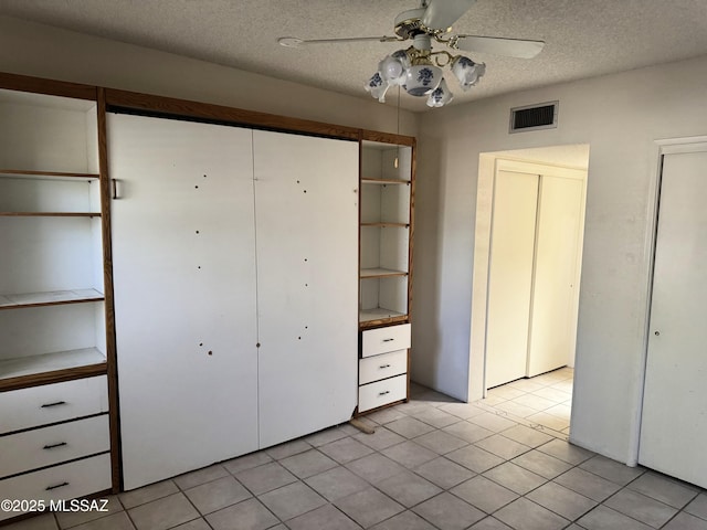 unfurnished bedroom featuring a ceiling fan, a textured ceiling, a closet, light tile patterned floors, and visible vents