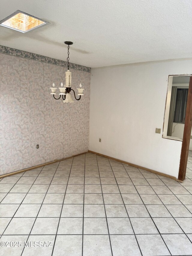 unfurnished room featuring wallpapered walls, a skylight, baseboards, a textured ceiling, and a notable chandelier
