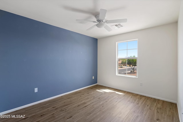 spare room with baseboards, a ceiling fan, wood finished floors, and visible vents