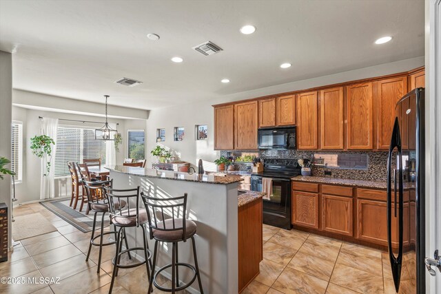 9224 S Big Tree Ln, Tucson, AZ 85756 - kitchen featuring visible vents, brown cabinetry, a kitchen island with sink, and black appliances