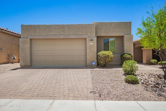 pueblo-style home featuring stucco siding, decorative driveway, and an attached garage