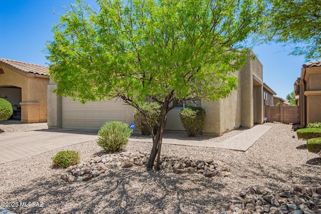 view of front of home featuring driveway, a garage, stucco siding, and fence