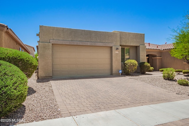 southwest-style home featuring an attached garage, decorative driveway, stucco siding, and a tiled roof