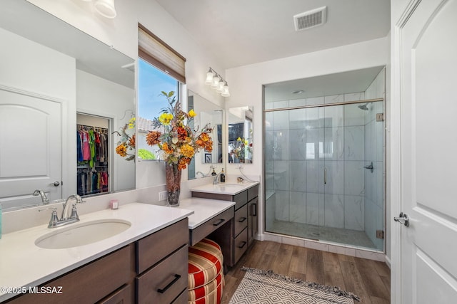 full bathroom with a shower stall, wood finished floors, a walk in closet, vanity, and visible vents