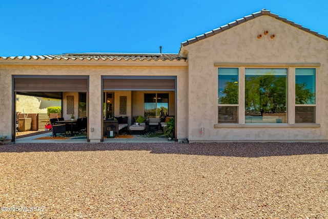 rear view of house featuring stucco siding, a tile roof, outdoor lounge area, and a patio