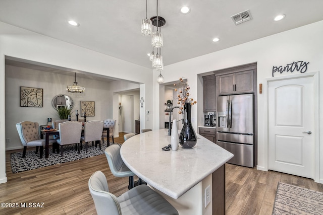 kitchen with decorative light fixtures, stainless steel fridge with ice dispenser, dark brown cabinets, and visible vents