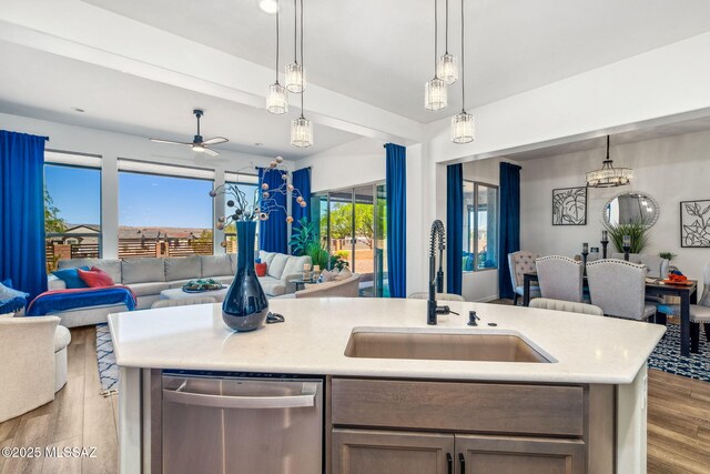 kitchen with light countertops, wood finished floors, stainless steel dishwasher, a sink, and open floor plan