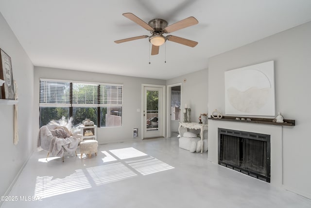 living room with baseboards, concrete flooring, ceiling fan, and a fireplace