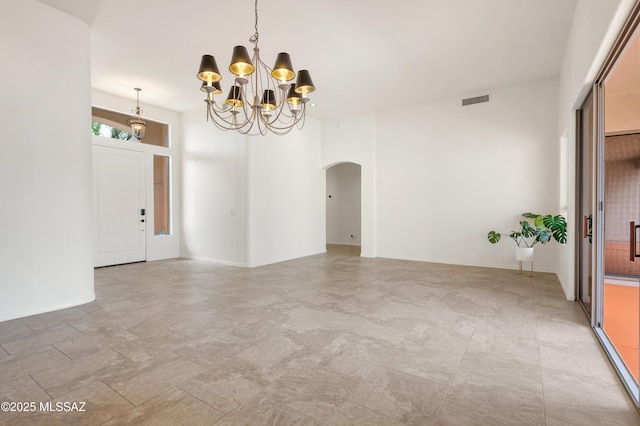empty room featuring a towering ceiling, arched walkways, visible vents, and a chandelier