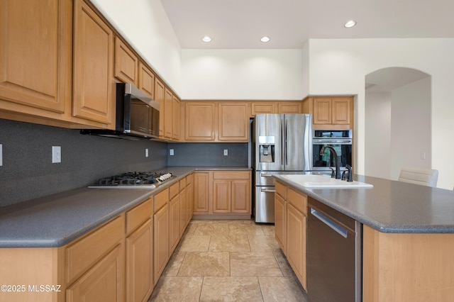 kitchen with tasteful backsplash, arched walkways, a kitchen island with sink, appliances with stainless steel finishes, and a sink
