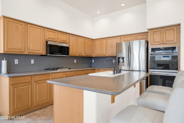 kitchen featuring tasteful backsplash, light tile patterned floors, appliances with stainless steel finishes, a sink, and a kitchen breakfast bar