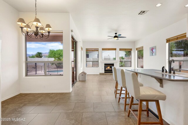 kitchen with recessed lighting, a sink, a glass covered fireplace, a breakfast bar, and ceiling fan with notable chandelier