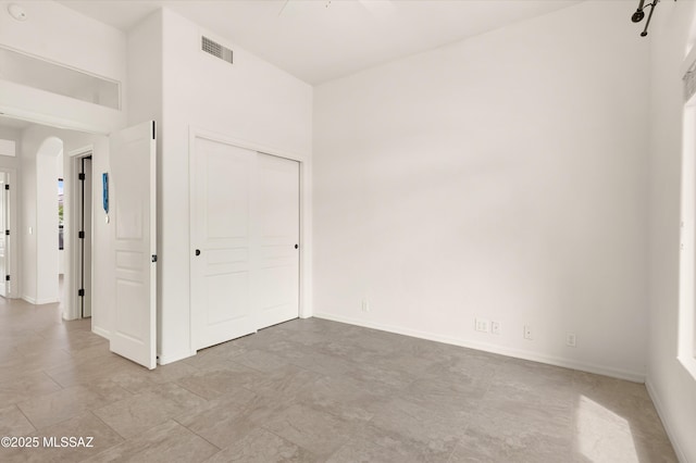 unfurnished bedroom with baseboards, visible vents, arched walkways, and a closet