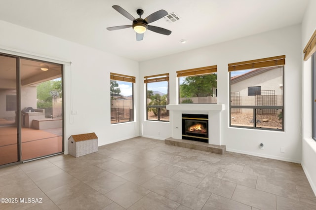 unfurnished living room featuring a glass covered fireplace, visible vents, ceiling fan, and plenty of natural light