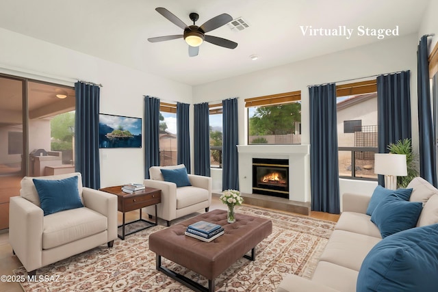 living area featuring ceiling fan, a glass covered fireplace, visible vents, and a healthy amount of sunlight