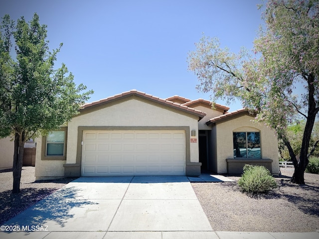 view of front of house featuring stucco siding, driveway, a tile roof, and a garage