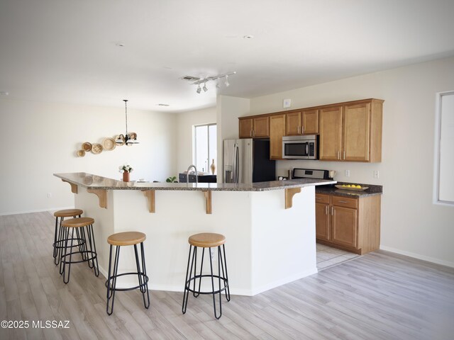 kitchen with a breakfast bar area, brown cabinetry, dark stone countertops, light wood finished floors, and stainless steel appliances