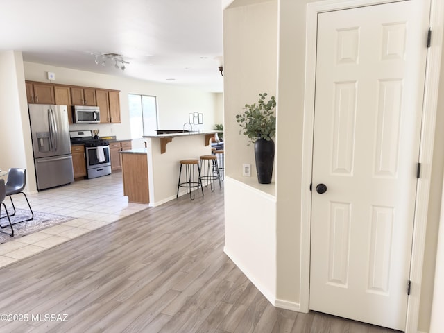 kitchen with a breakfast bar area, brown cabinetry, baseboards, stainless steel appliances, and light wood-style flooring