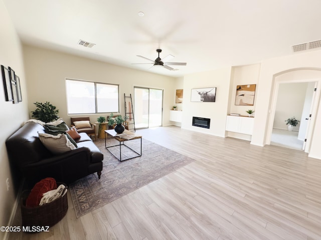 living room with visible vents, a ceiling fan, light wood finished floors, and arched walkways
