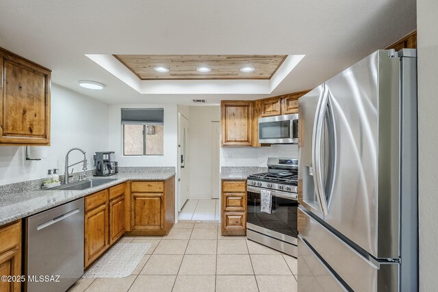 kitchen featuring a tray ceiling, brown cabinetry, a sink, and appliances with stainless steel finishes