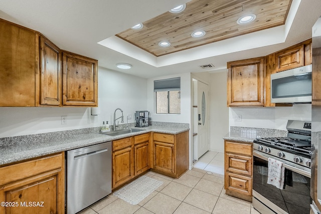kitchen with brown cabinetry, visible vents, a sink, a raised ceiling, and stainless steel appliances