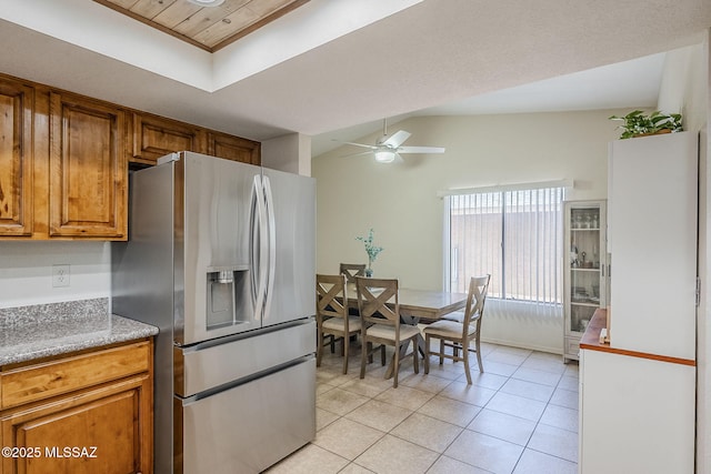 kitchen featuring brown cabinetry, vaulted ceiling, ceiling fan, light tile patterned floors, and stainless steel fridge with ice dispenser