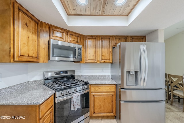 kitchen with appliances with stainless steel finishes, brown cabinetry, a raised ceiling, and recessed lighting