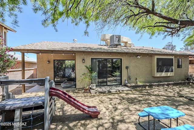 rear view of property with fence, a patio, stucco siding, central AC unit, and a shingled roof