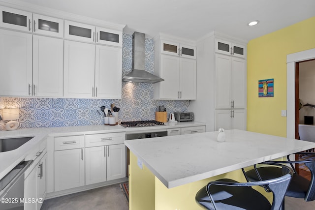 kitchen featuring wall chimney range hood, a kitchen breakfast bar, white cabinetry, backsplash, and a kitchen island