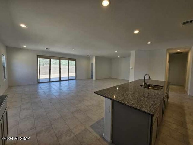 kitchen featuring an island with sink, dark stone countertops, visible vents, a sink, and open floor plan