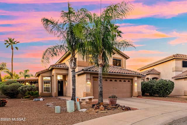 view of front facade with stucco siding, driveway, a tile roof, and a garage