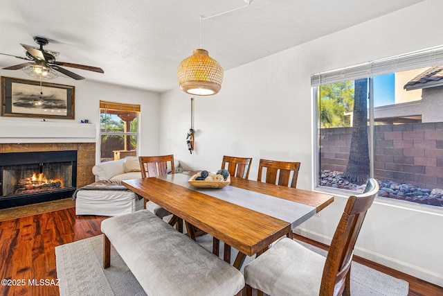dining room featuring baseboards, a ceiling fan, a warm lit fireplace, and wood finished floors