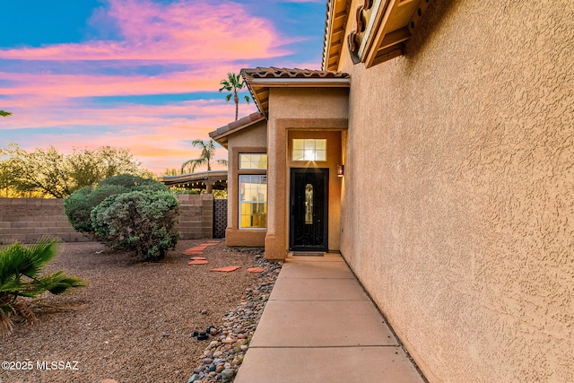 view of exterior entry featuring fence, stucco siding, and a tile roof