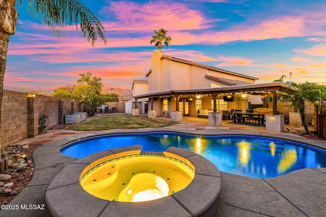 pool at dusk with a fenced backyard, outdoor dry bar, a pool with connected hot tub, and a patio area