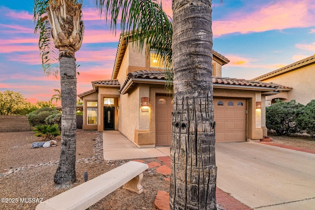 view of front of home featuring a garage, driveway, a tile roof, and stucco siding