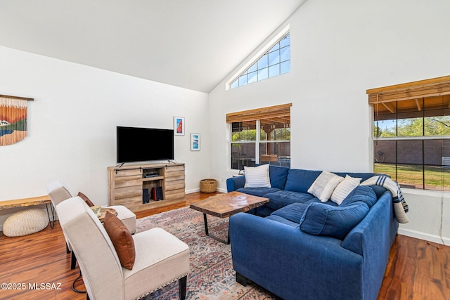living area with plenty of natural light, baseboards, wood finished floors, and high vaulted ceiling