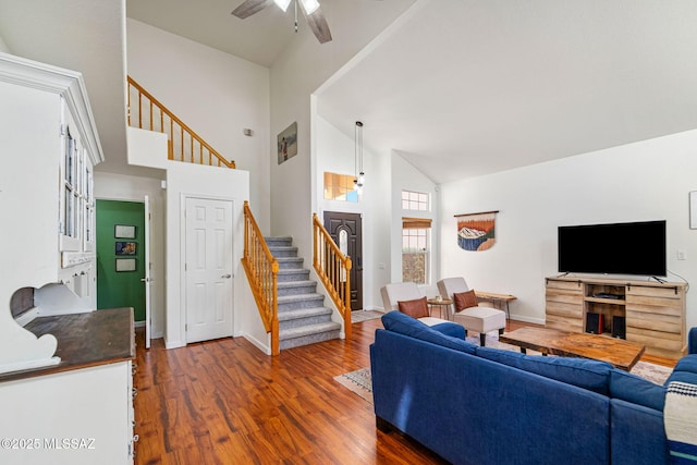 living area featuring stairs, baseboards, dark wood-style floors, high vaulted ceiling, and a ceiling fan