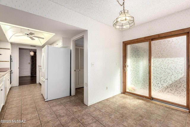 unfurnished dining area with light tile patterned floors, ceiling fan, wallpapered walls, and a textured ceiling