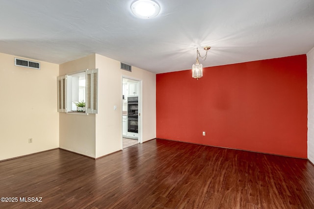 spare room featuring a notable chandelier, wood finished floors, and visible vents