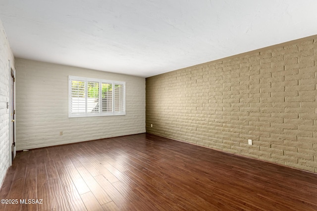 unfurnished room with brick wall and wood finished floors